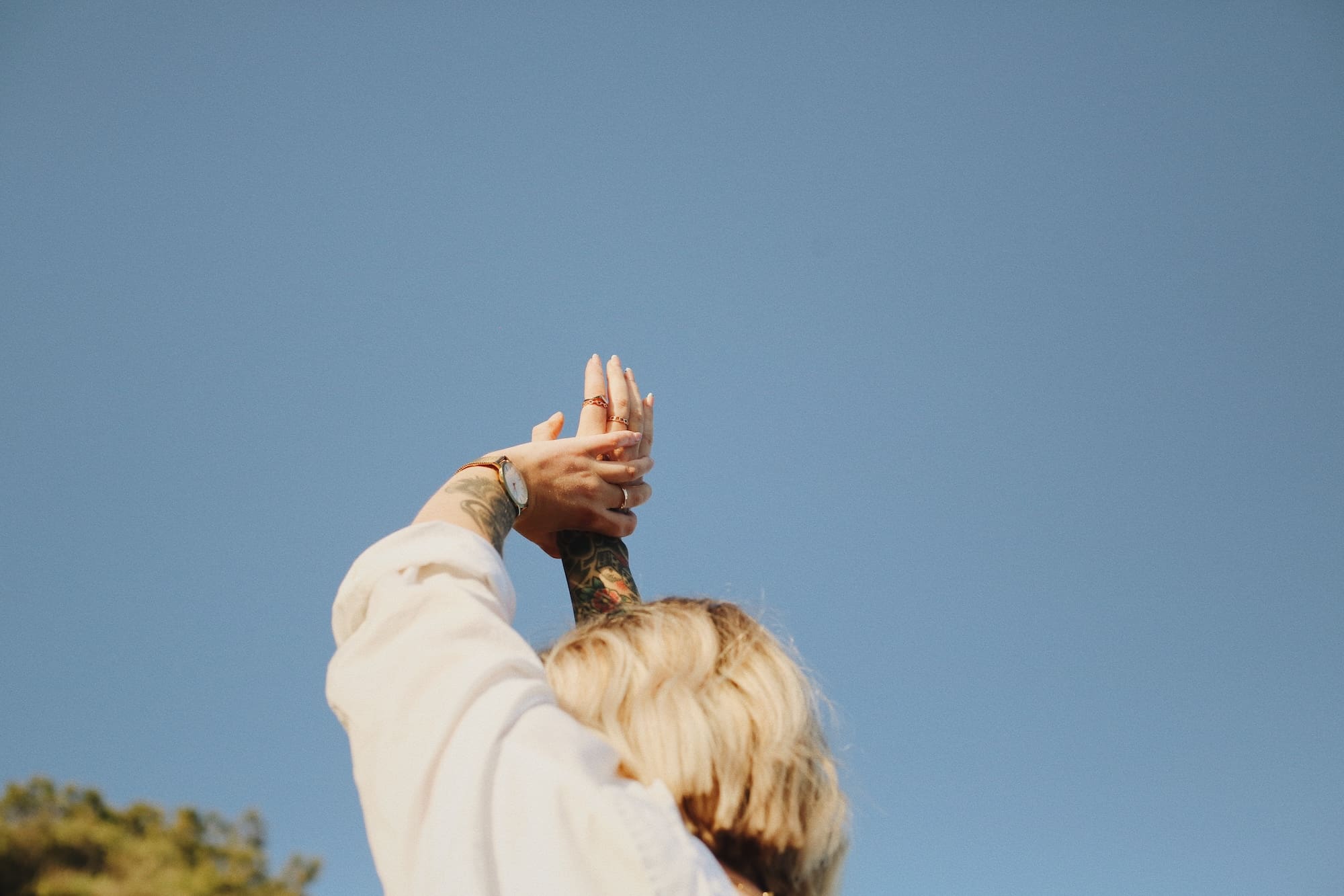 Person with blonde hair stretching their arms overhead against a clear blue sky.