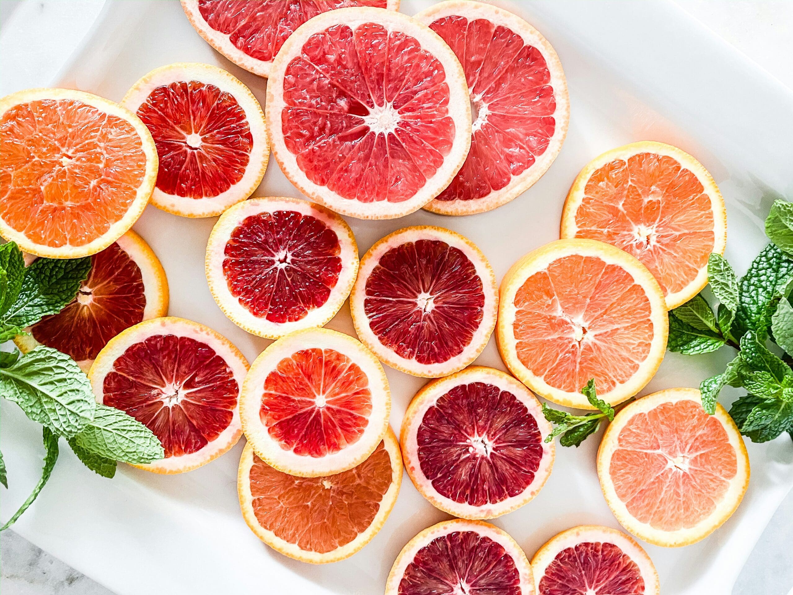 Slices of pink and red citrus fruit arranged on a white platter with fresh mint leaves.